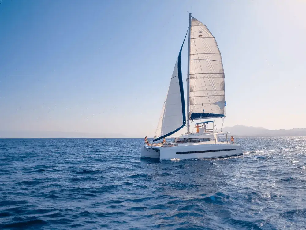 A sailing catamaran in blue waters with a group of people on a private premium sailing holiday int the Mediterranean.