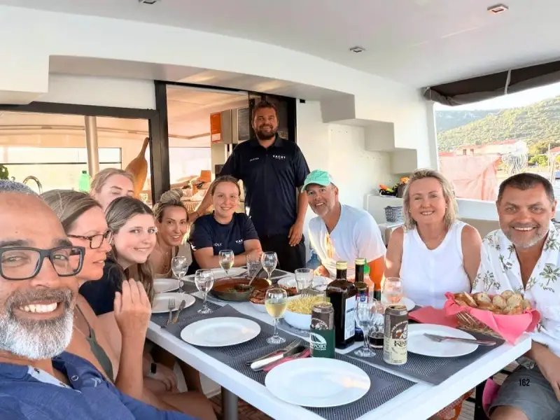 Yacht Getaways guests enjoying a shared meal with their skipper and host aboard a luxury catamaran during a Mediterranean sailing holiday, highlighting the crew and guest experience behind the company’s 2026 Best Yacht Cruises nomination.
