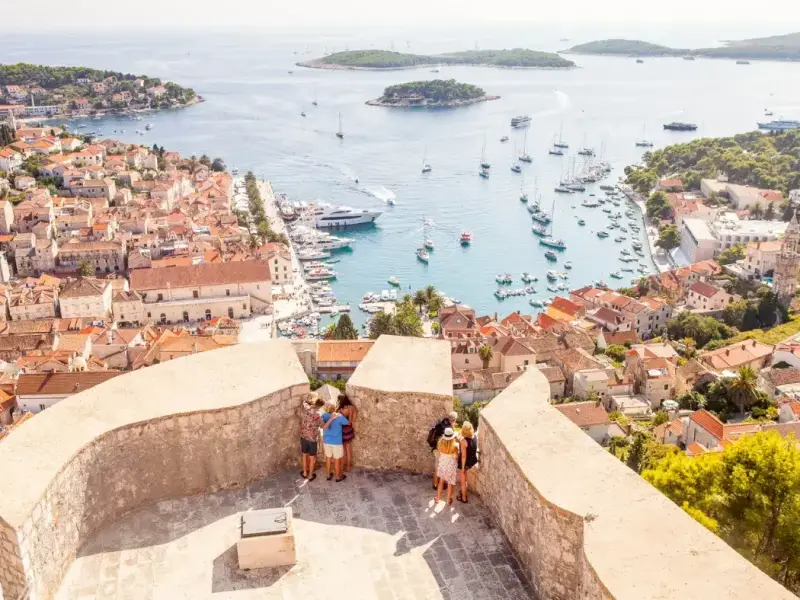 High viewpoint above a lively Croatian harbour filled with anchored yachts and boats, with an old town of terracotta rooftops on one side and small Adriatic islands offshore — perfect for a 2026 guide to Croatia’s best places to visit, especially Hvar and nearby island-hopping highlights.