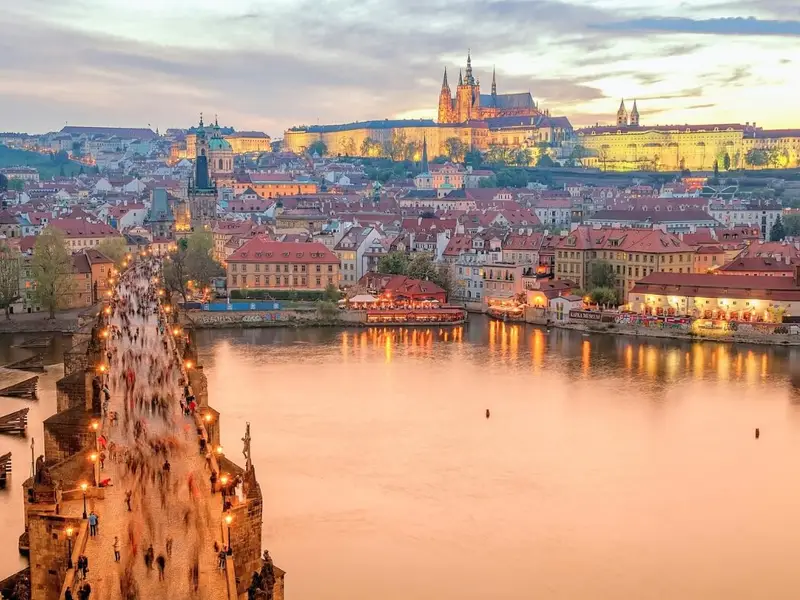 Sunset view over Prague, Czechia, with crowds crossing Charles Bridge above the River Vltava and Prague Castle glowing on the hill in the background. A classic Prague city-break scene that works well for an article on the safest places to visit in Europe, reflecting Czechia’s reputation as a stable, visitor-friendly destination where most travel feels easy, walkable, and low-stress beyond the usual busy tourist spots.