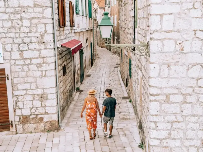 Couple walking through a narrow limestone street in Dubrovnik Old Town, Croatia, surrounded by historic stone buildings and traditional Mediterranean architecture. Exploring these quiet streets is one of the most enjoyable ways to experience Dubrovnik, where centuries-old walls, lanterns and winding alleys reveal the timeless charm of the UNESCO-listed city.