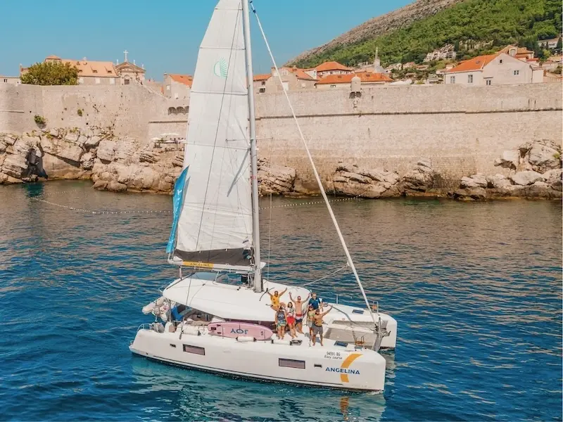 Aerial photo of a luxury catamaran in front of the walls of Durbrovnik with a group of people as they sail Croatia on a 2026 catamaran cruise.
