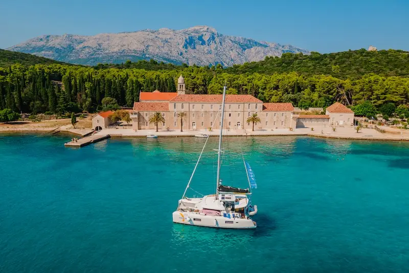 Aerial photo of a luxury Bali 4.5 catamaran anchored in a blue bay at Badija Monastery, Korcula, in Croatia.