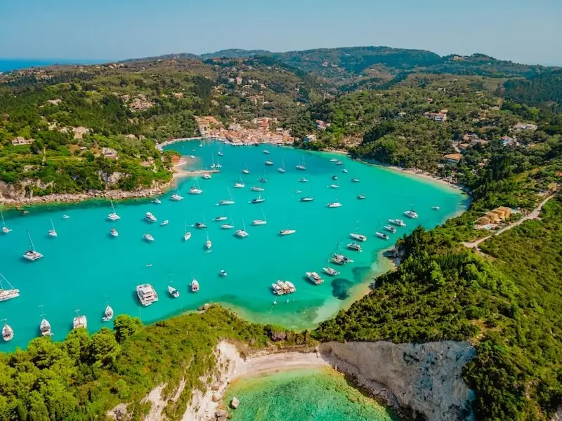 Aerial view of yachts anchored in the turquoise bay of Lakka, Paxos Island, Greece, surrounded by lush hills and Ionian villages — a signature stop on luxury catamaran cruises with Yacht Getaways.