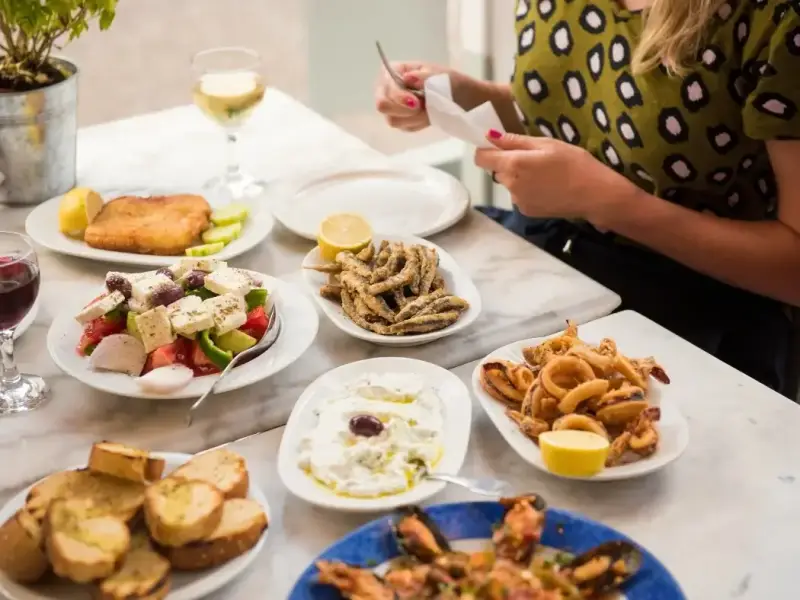 Traditional Greek dishes served at a taverna in Athens, including Greek salad, fried seafood, dips, toasted bread, and wine on a marble table. This image works well in an Athens, Greece travel guide focused on local food, authentic dining experiences, and the best things to do in Athens beyond the major landmarks, especially for travellers who want to enjoy the city through its restaurants and Mediterranean flavours.