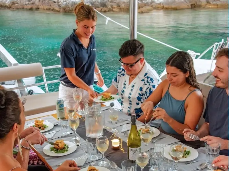 Yacht Getaways host serving a freshly prepared Mediterranean dinner to guests onboard, showcasing five-star service and fine dining on a luxury catamaran.