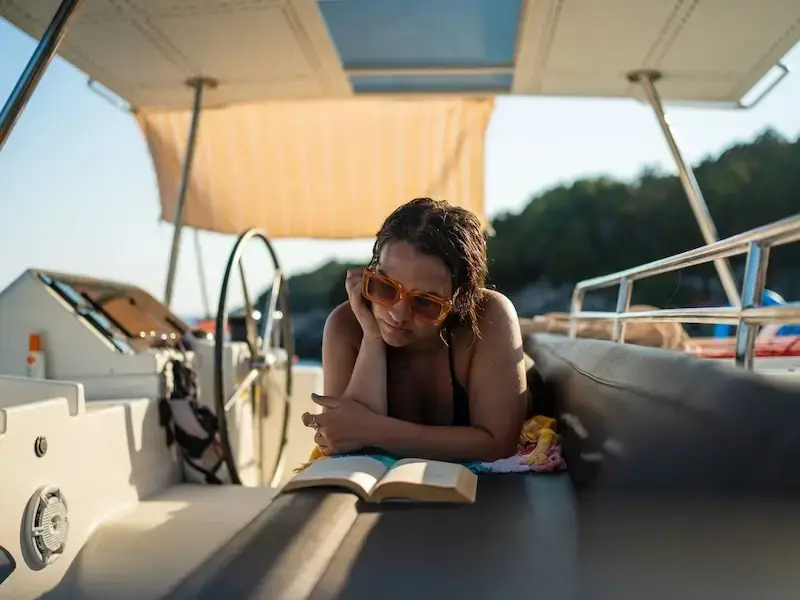 A girl lays on a luxury catamaran reading a book at golden hour while on a chart yacht cruise.