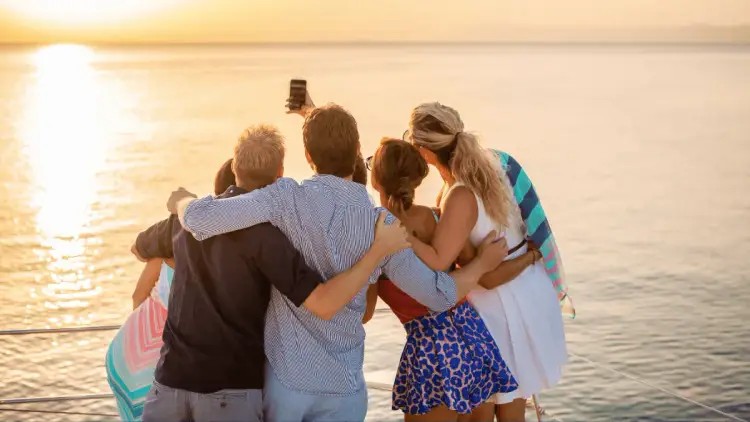 Group of people on a private yacht sailing holiday in the Mediterranean taking a selfie together on the bow of a premium catamaran at sunset.