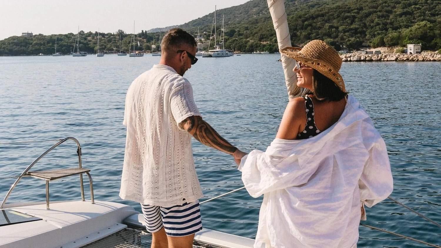 Couple holding hands on the deck of a luxury catamaran sailing through calm Mediterranean waters — enjoying a Yacht Getaways luxury sailing holiday in Greece and Croatia.