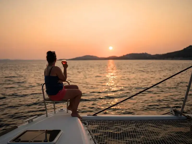 A beautiful golden sunset over the Mediterranean with a woman sitting on the bow with a glass of wine while relaxing on a catamaran cruise.