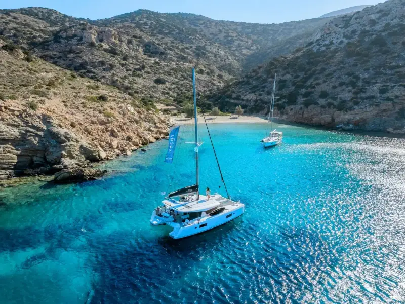 A catamaran anchored in a secluded Mediterranean bay with clear turquoise water, rocky hills and a quiet beach, capturing the restorative appeal of blue health travel. This image reflects the calm and natural beauty of a luxury yacht holiday in Greece or Croatia, where guests can swim, slow down and reconnect with the sea away from crowded resorts.