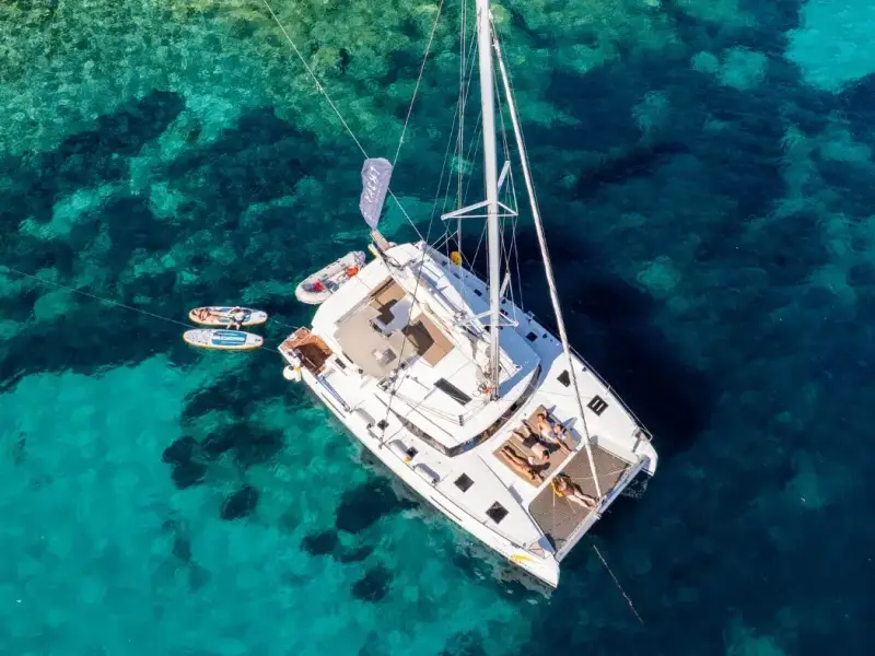 Aerial view of a white catamaran anchored over crystal-clear turquoise water in Croatia, with paddleboards floating nearby and reef patterns visible below — an ideal visual for a 2026 Croatia islands travel guide, capturing the slow-luxury style of sailing, swimming stops and relaxed days that Yacht Getaways guests look for.