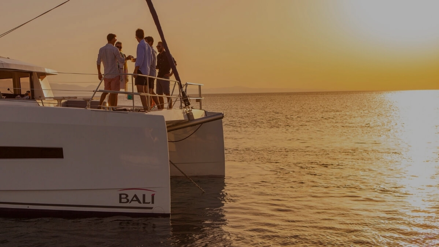 Group of friends enjoying sunset together aboard a private catamaran during a Mediterranean sailing holiday with Yacht Getaways.