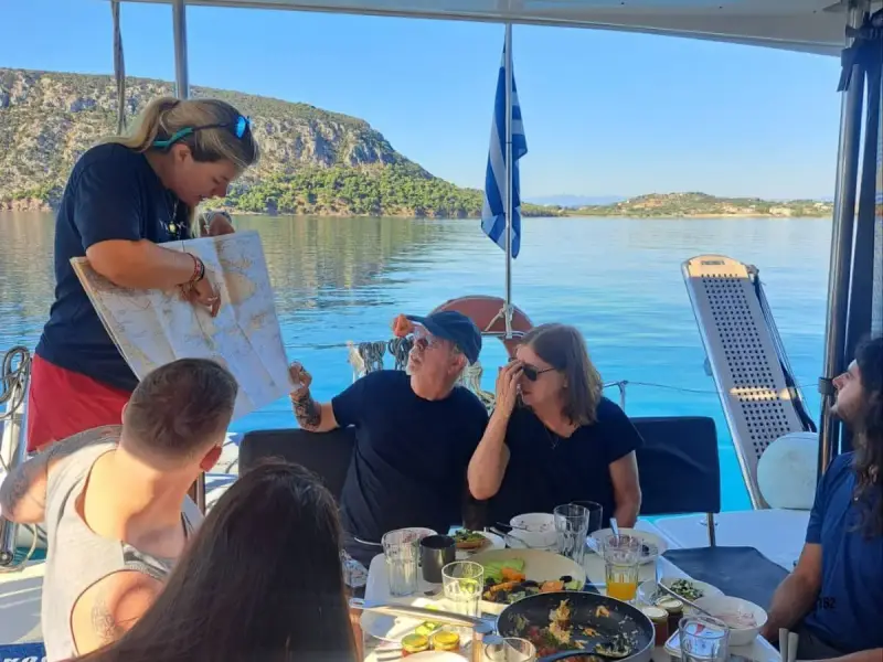 Yacht Getaways host sharing a sailing map with guests over breakfast aboard a luxury catamaran in Greece, showing the personal crew service and small-group experience behind Yacht Getaways’ 2026 Best Yacht Cruises nomination.