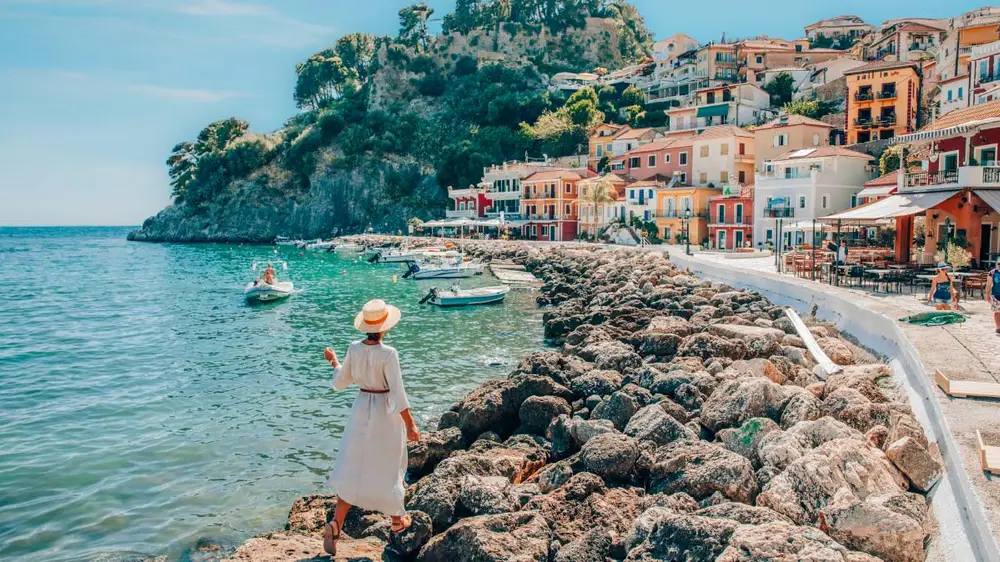 Parga town with colourful villas and Venetian architecture with a woman standing on the rocky shoreline while on a luxury sailing holiday in the Ionian.