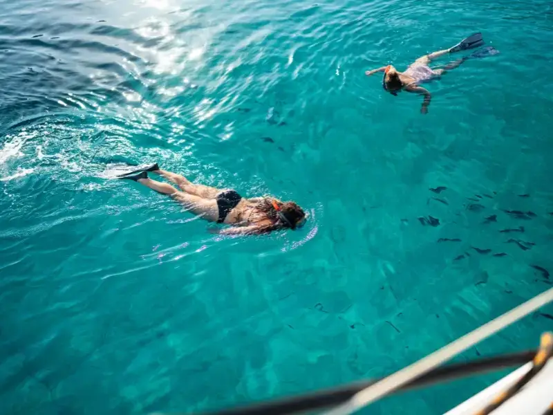 Guests snorkelling in clear blue water beside a catamaran on a Yacht Getaways trip, supporting responsible travel standards as a B Corp Certified company.