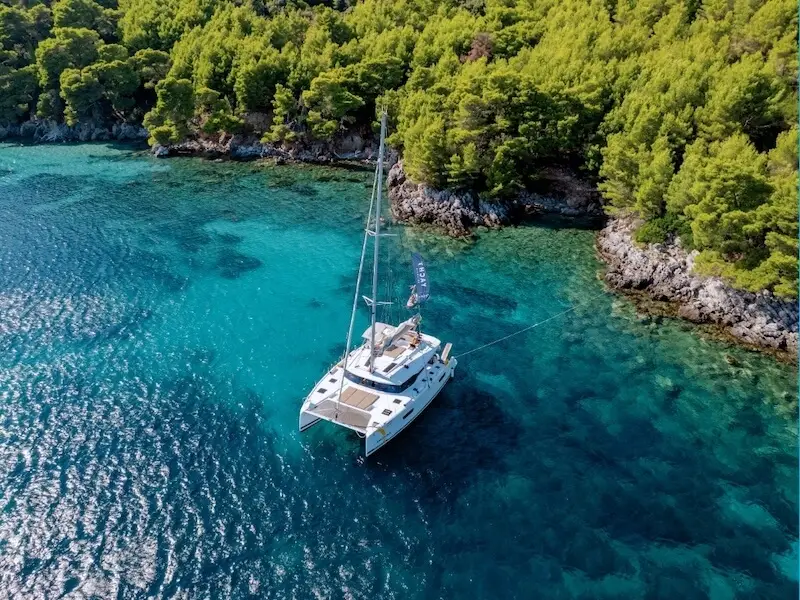 A Yacht Getaways catamaran anchored in a turquoise cove surrounded by pine forests in Croatia, highlighting the beauty of small-group sailing holidays.