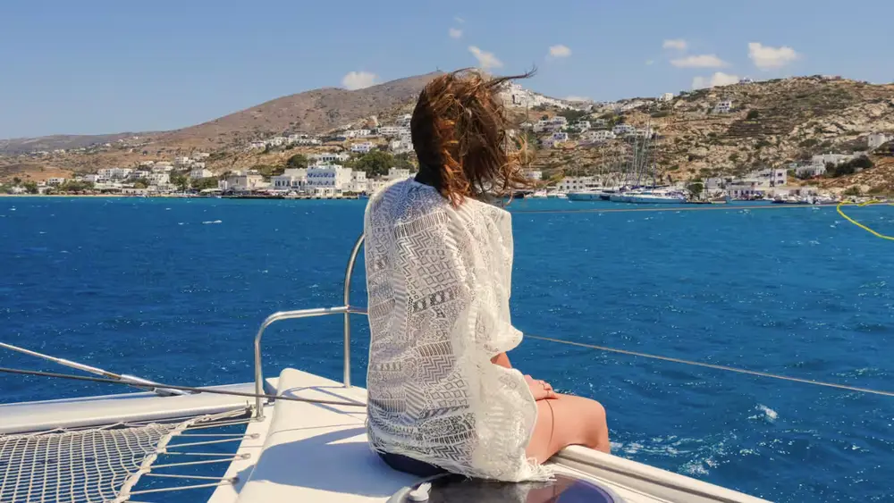 Guest relaxing on the bow of a catamaran while sailing towards a whitewashed Cyclades island during a luxury Greece yacht holiday.