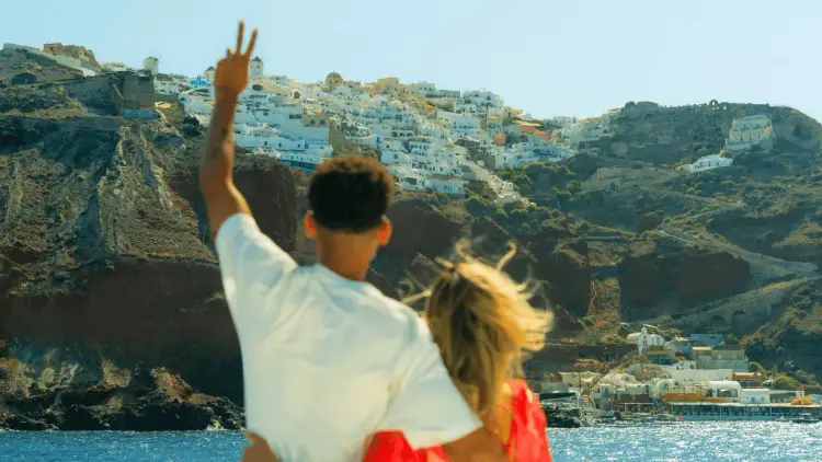 Couple embracing aboard a yacht while approaching Paros, Greece, with the island's iconic whitewashed villages and traditional windmills overlooking the Aegean Sea.
