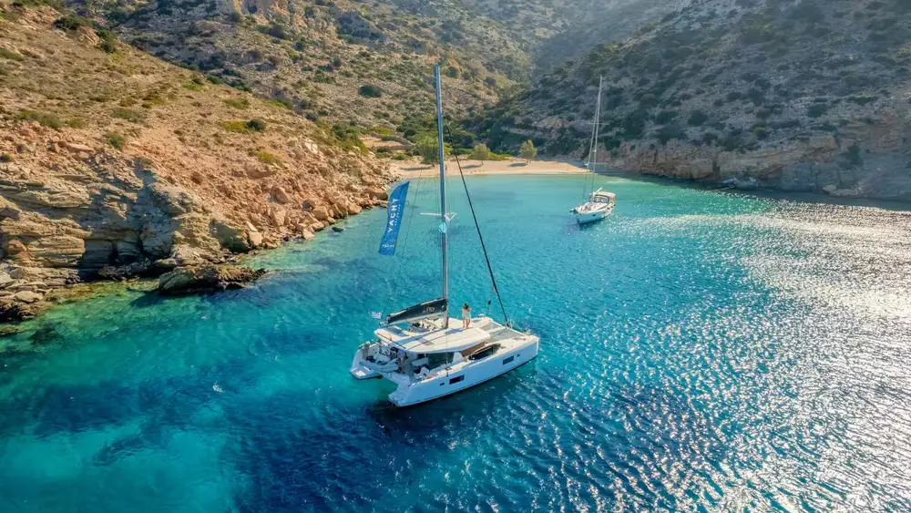 Luxury catamaran anchored in a secluded turquoise bay surrounded by rocky Cyclades scenery during a Greek island sailing holiday.