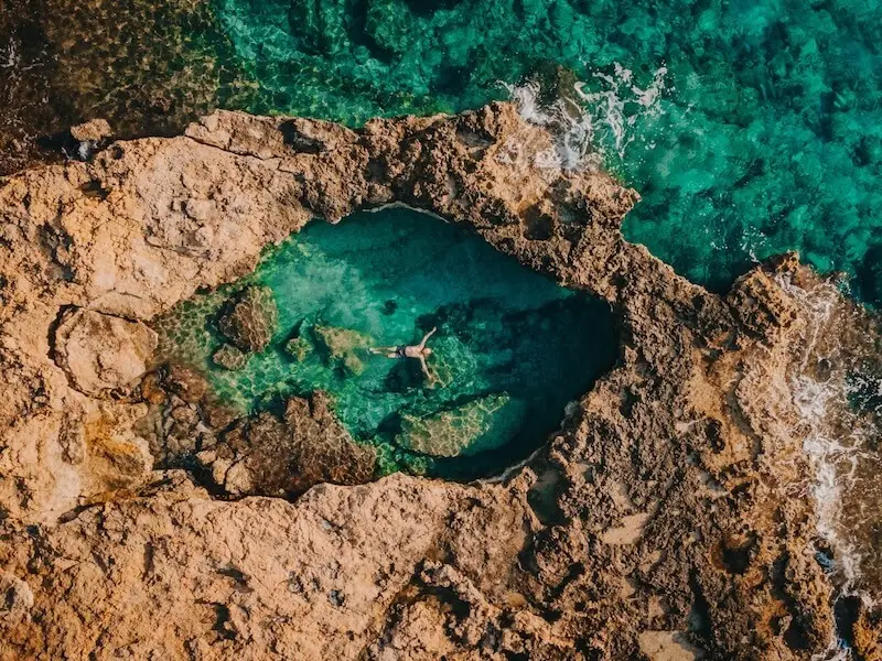 Aerial view of a traveller relaxing in a natural rock pool on Koufonisia Island, Greece, surrounded by turquoise Cycladic waters — a serene escape for luxury travellers and catamaran sailing holidays with Yacht Getaways.
