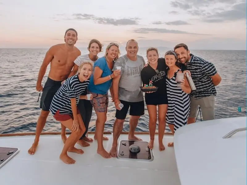 Happy Yacht Getaways guests celebrating together on a luxury catamaran at sunset during a Mediterranean sailing holiday in Greece or Croatia.