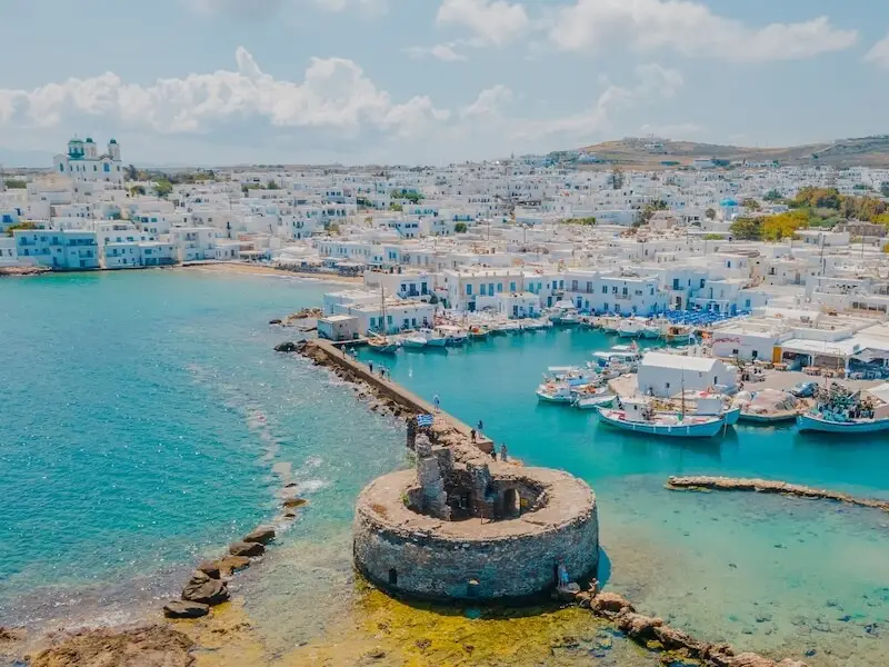 Aerial view of Naoussa harbour in Paros, Greece, featuring whitewashed Cycladic buildings and turquoise waters — a favourite destination for luxury travellers and catamaran cruises with Yacht Getaways.