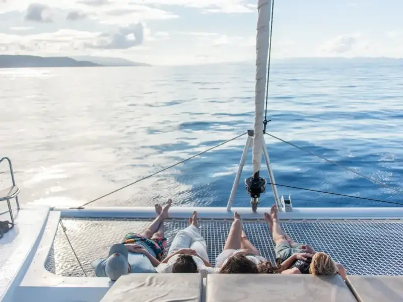 Travellers relaxing on the front deck of a catamaran sailing through the Greek islands, with open sea views and calm Mediterranean waters. This image fits an Athens, Greece travel guide that transitions into a Greek island sailing holiday, highlighting the experience of moving from an Athens city break to a luxury catamaran cruise around Greece.