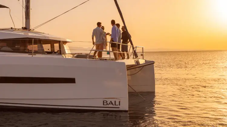 A group of friends on a private premium catamaran sailing holiday in the Mediterranean talking and connecting on the bow of the yacht at sunset.