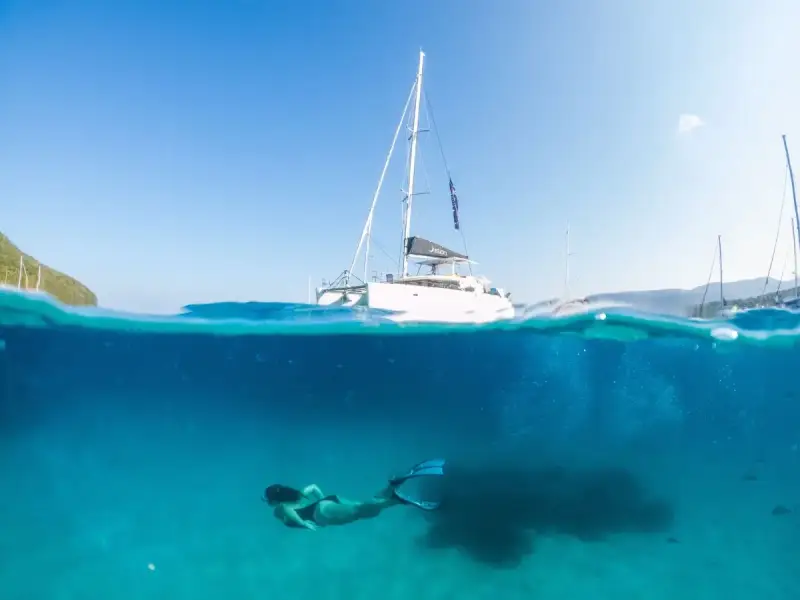 An overhead view of a traveller lying on a paddleboard in clear blue-green water, showing the calm and restorative side of a Mediterranean yacht holiday. The image reflects blue health travel through gentle movement, sunlight, open water and quiet moments at sea, ideal for a wellness-inspired catamaran cruise in Greece or Croatia.