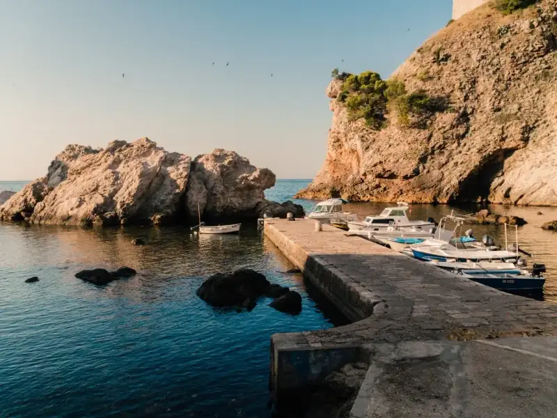 A peaceful rocky bay on the Dubrovnik coast in Croatia, with small boats moored beside a stone jetty and calm Adriatic water below steep coastal cliffs. This image captures the quieter side of Dubrovnik travel and reflects why the city is so appealing for a Croatia holiday, with scenic coastal views, hidden corners and easy access to the sea beyond the Old Town. This is also a Game of Thrones film location used in the Battle of Black Water Bay.
