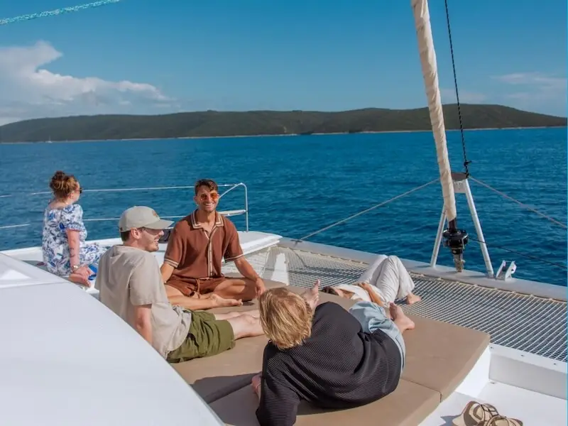 Group of travellers relaxing on deck during a Yacht Getaways catamaran cruise along the Croatian coast, surrounded by calm blue water and sunshine.