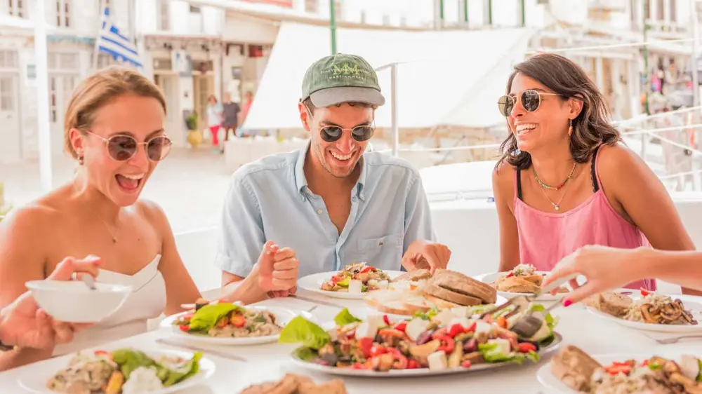Greek mezze feast with travellers laughing and happy just before diving into all of the Greek cuisine.