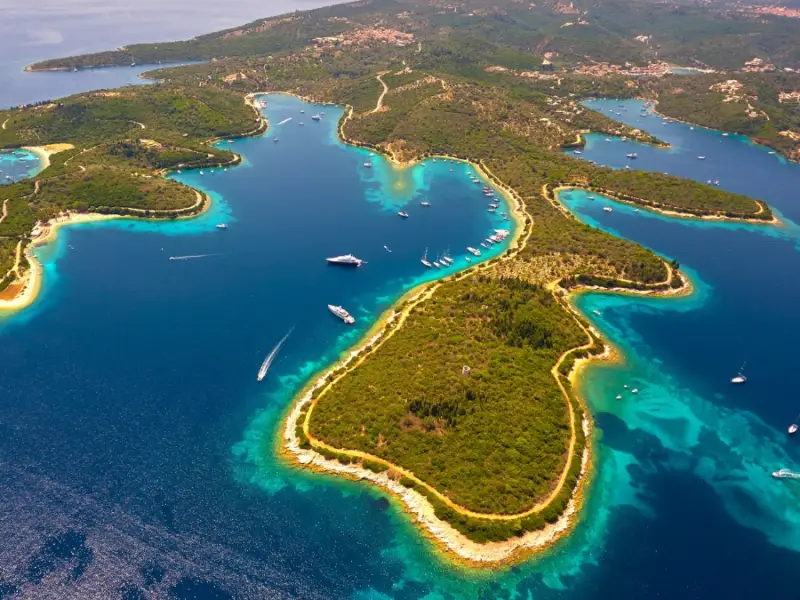 Aerial image of Spilia Bay on Meganisi, showing its curved coastline, emerald-green water, and multiple sheltered inlets surrounded by lush greenery. This beautiful Ionian bay is best reached by boat and is known for its peaceful anchorage, scenic swimming spots, and relaxed atmosphere on a Greece yacht cruise.