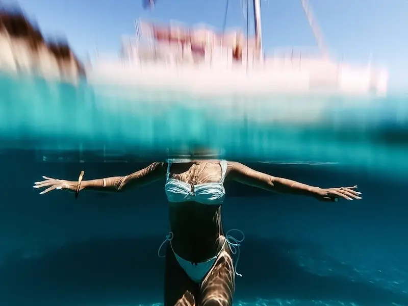 A photo of a woman partially submerged in turquoise waters while sailing Croatia on a luxury catamaran enjoying life.