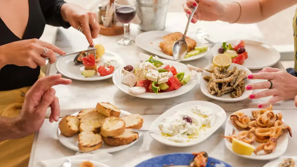Guests sharing traditional Greek dishes including Greek salad, seafood and mezze during a luxury sailing holiday through the Saronic Gulf islands.