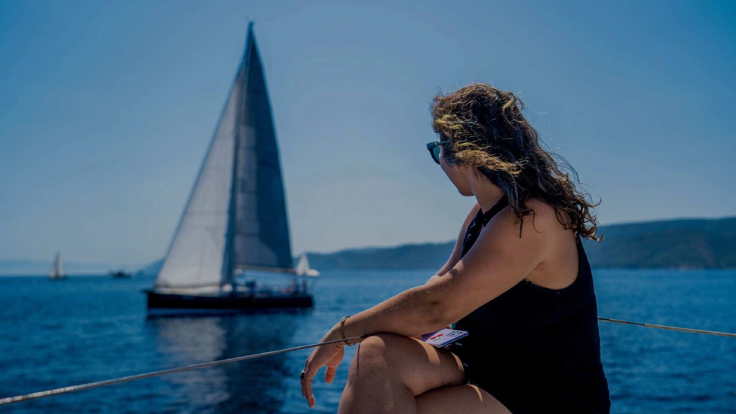 Woman sitting on bow of a catamaran looking at another yacht