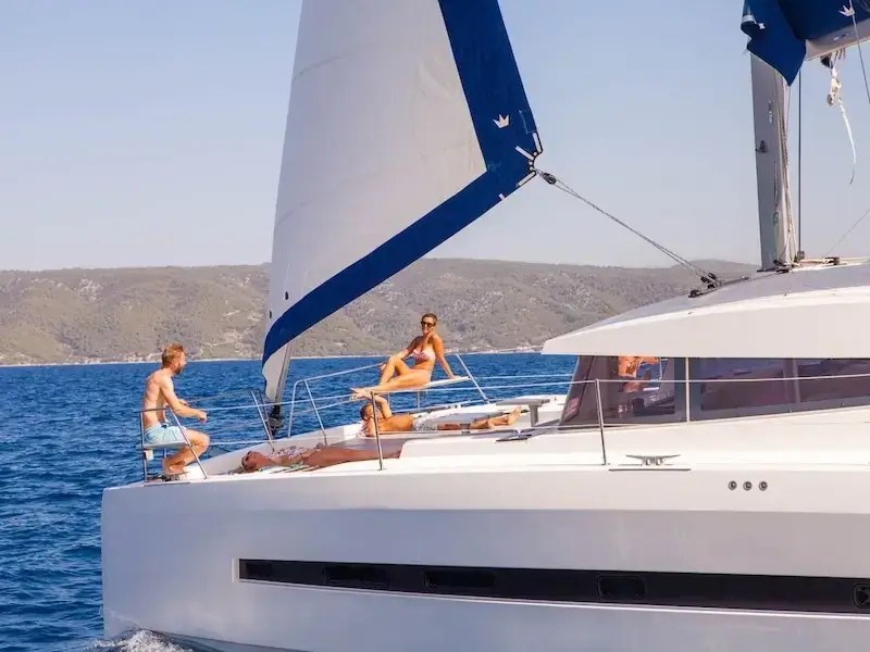 A group of luxury travellers sit on a catamaran and relax on a sailing holiday in the Mediterranean.