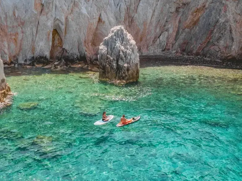 A couple float in a beautiful blue bay surrounded by rugged coastline in the Mediterranean while on a relaxing luxury catamaran cruise with yacht Getaways.