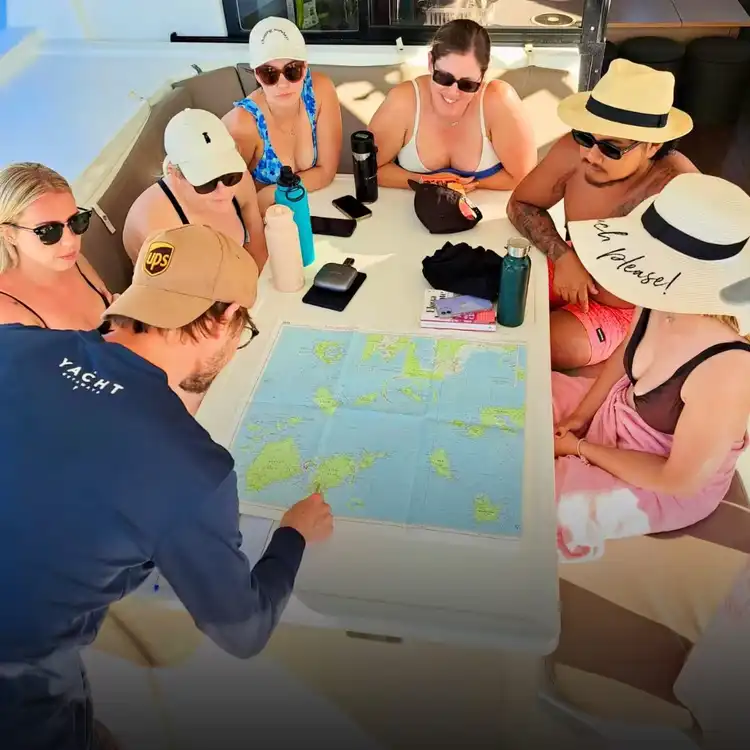 Yacht Getaways skipper briefing guests on the day's sailing route using a nautical chart aboard a Greek island catamaran charter.