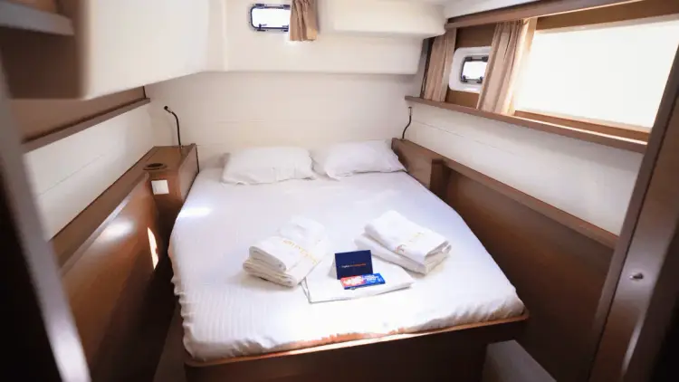 Bright, comfortable double cabin aboard a Yacht Getaways premium catamaran, featuring a neatly made bed, fresh towels, bedside storage and windows for natural light on a Mediterranean family sailing holiday.