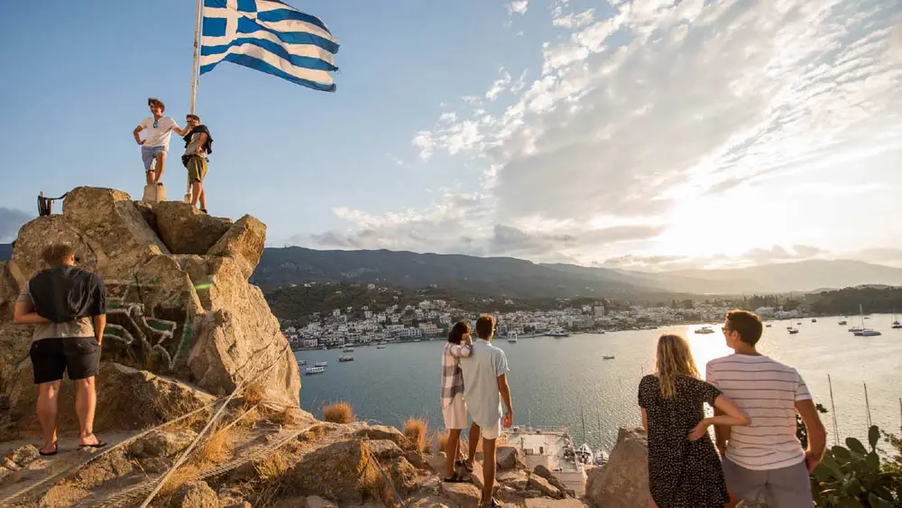 People standing at the flag and clocktower of Poros at sunset.
