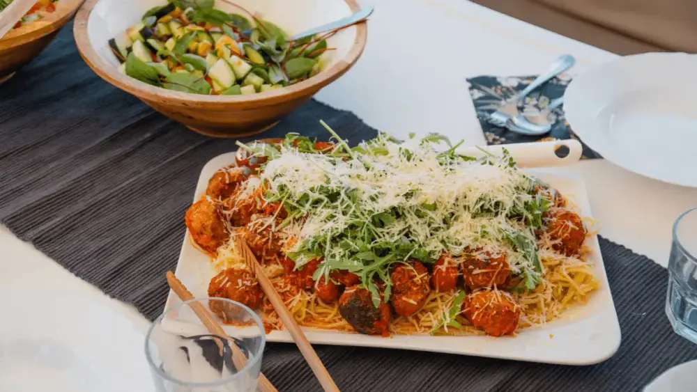 Freshly prepared spaghetti with tomato sauce, meatballs, grated cheese and rocket, served alongside a colourful salad on the dining table of a sailing catamaran.