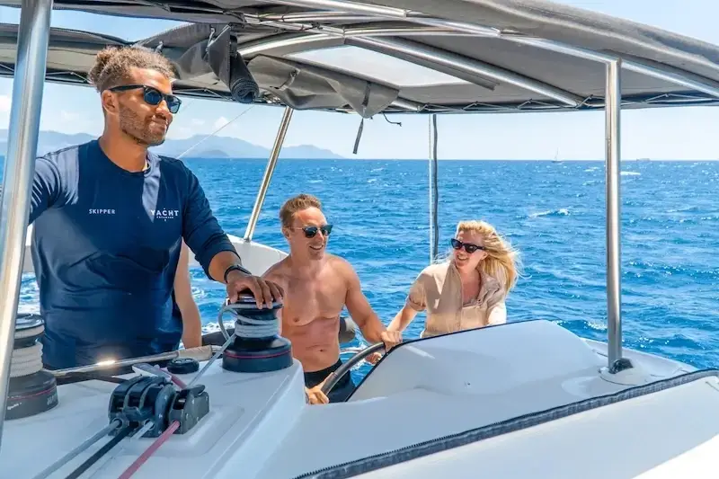 A couple smiles while learning to sail on their luxury holiday aboard a catamaran in the Mediterranean.