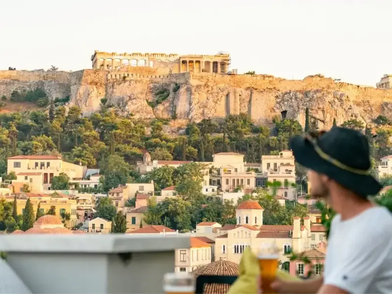 Traveller enjoying drinks on a rooftop terrace with a view of the Acropolis in Athens, Greece. This photo captures the relaxed atmosphere of an Athens city break and fits an Athens travel guide focused on rooftop bars, sunset views, neighbourhood charm, and stylish experiences before continuing on to the Greek islands.