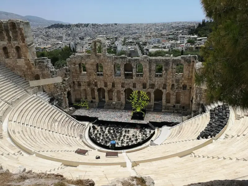 The Odeon of Herodes Atticus, an ancient stone theatre beneath the Acropolis in Athens, Greece, set up for a live performance with seating and stage visible. This image is ideal for an Athens travel guide covering cultural experiences, historic landmarks, and evening activities, including concerts and performances in one of the most iconic open-air theatres in the Mediterranean.