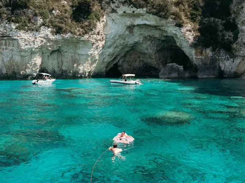 A bright blue Greek island bay with a sea cave and people swimming in seclusion while on a luxury cruise. 