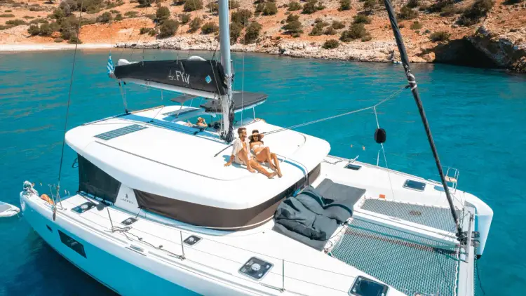 Couple relaxing together on the spacious upper deck of a premium sailing catamaran anchored in a secluded Greek island bay, surrounded by turquoise Mediterranean waters.