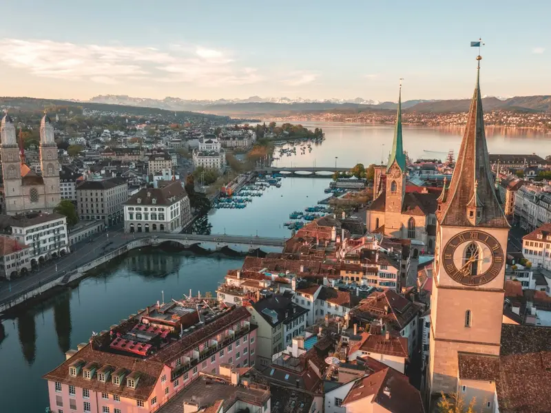 Aerial view over Zurich’s Old Town in Switzerland, with church spires and the Limmat River leading towards Lake Zurich at sunrise, and the Alps faintly visible in the distance. A calm, beautifully organised city scene that fits an article on the safest places to visit in Europe, reflecting Switzerland’s reputation for stability, excellent public transport, and an easy, low-stress travel experience for mature travellers.