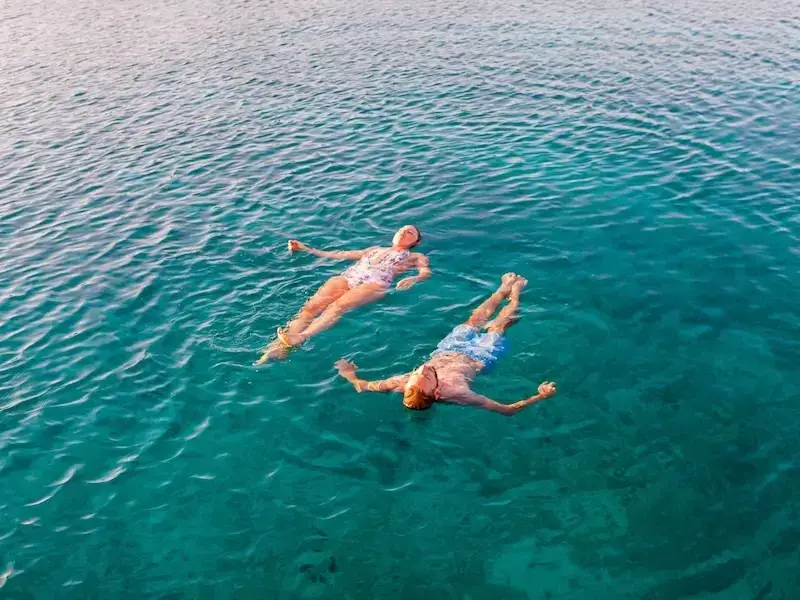 A couple floats in turquoise waters in the Mediterranean while looking at peace on a catamaran cruise.